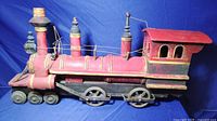 Side view of the large wooden toy train engine showing hand painted red and yellow details and metal wheels.
