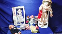 Full view of the vintage doll collection including boxed Mademoiselle Eugene doll, three small dolls in package, larger porcelain doll on stand, and other assorted dolls with moving eyes.