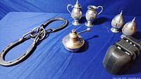 Wide view of the lot showing two pairs of salt and pepper shakers, small oil lamp, black metal utensil sharpener, and large horseshoe puzzle on blue fabric background.