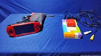 Red PSP 3000 console, carrying case, charging cable, and Tetris plug-and-play device with cables
