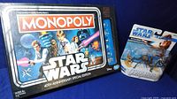 Photo showing Star Wars Monopoly 40th Anniversary Special Edition game in tin box alongside Star Wars Unleashed Battle Packs packaged toy