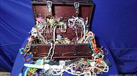 Photo showing treasure chest filled and overflowing with assorted costume jewelry pieces, beads, necklaces, bracelets, and watches
