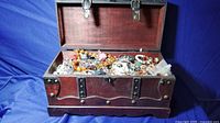 Photo of open wooden chest showing wide assortment of mixed jewelry including necklaces, rings, bracelets and earrings
