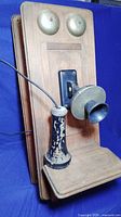 Front angle of vintage wooden wall-mounted telephone showing metal bells, mouthpiece, and handset with paint wear