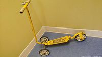 Full view of the vintage yellow three-wheeled scooter showing the handlebar, platform, and wheels.