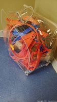 Clear plastic carrying case with orange and blue Hot Wheels track pieces inside, showing loop and curved track sections.