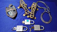 Top view of the iron eagle door knocker, shoe shine foot plates, horseshoe with chain, and three antique padlocks with keys arranged on blue cloth