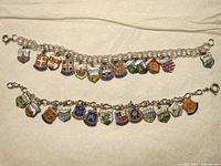 Top and bottom view of two charm bracelets displaying colorful enamel shield charms on chain link bracelets, laid flat on light fabric background.