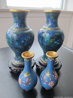 Photo showing four blue vases with floral and bird motif. Two larger vases have black stands, two smaller do not.