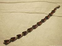Full view of the bracelet showing linked trapezoidal silver segments, each containing a rectangular amber stone, laid flat to show length and design.