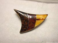 Front view of the brooch showing tri-coloured amber inlay with dark brown, reddish, and yellow amber segments in polished silver.