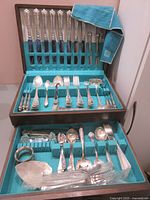 Wooden two-drawer chest with turquoise felt lining filled with assorted knives, forks, spoons and serving pieces