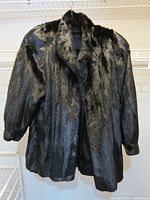 Photo of the black mink fur coat displayed on a hanger showing front and sleeve details, highlighting texture and length.