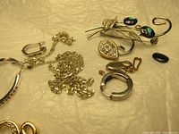 Photo showing assortment of broken jewelry including brooch, chain, clasps, and loose beads on a beige textured surface.
