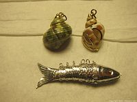 Top view of two shell pendants and one fish-shaped silver-tone pendant, showing details and size