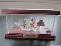 Front view of glass ship model inside wooden and glass display case with British flag label
