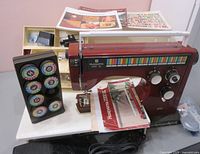 Red Husqvarna 2000 SL sewing machine featuring colorful stitch pattern selector. Black holder with multiple stitch cartridges displayed on left side. Instruction manuals placed on machine base.