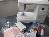 Front view of Janome sewing machine with foot pedal, spool holders, instruction library booklet and bag of threads