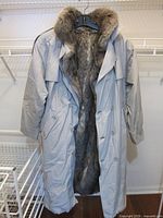 Photo of taupe men's full-length coat with fur lining and collar shown on hanger, front view.