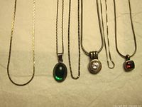 Six silver chains with various pendants arranged side by side on a cloth background.