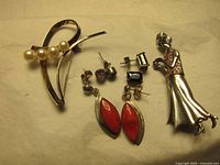 Various silver jewelry items including female figure pin, pearl brooch, red drop earrings, and small studs