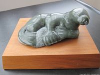 Photo of a grey soapstone seal sculpture resting on a wooden display stand. The seal is smooth and polished with detailed flippers and face.