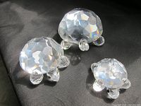 Photo of three transparent Swarovski turtle figurines with faceted crystal shells on a black surface showing largest approximately 3 inches long.