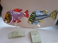 Pair of crystal fish figurines on metal stands side by side against neutral background.