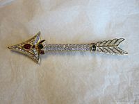 Front view of the gold tone arrow brooch with multi-coloured crystals showing clear, red, and green stones.