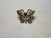 Front view of the butterfly brooch showing gold-tone metal with blue, green, and clear crystals.