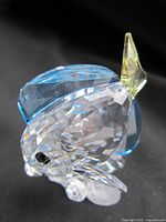 Close-up side view of Swarovski crystal fish figurine showing blue upper fin, yellow tail fin, clear faceted body with frosted effect, and black eye.