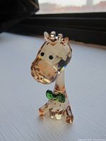 Front view of the light brown Swarovski crystal giraffe figurine with green bow tie on a white surface near a window