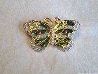 Front view of gold tone butterfly brooch with green enamel and clear and red crystals.