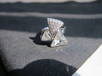 Close-up of silver-tone ring featuring three triangle crystals, sunlit on black fabric.