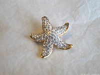 Front view of the starfish brooch showing the gold tone metal and clear crystals covering the entire front.