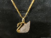 Close-up photo of the gold tone swan pendant with clear crystals on the body, showing one missing eye stone.