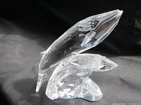 Crystal figurine of two whales, one larger and one smaller, with clear transparency and precision cut details, shown against a dark background to highlight clarity and craftsmanship.