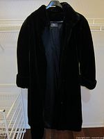 Front view of black faux fur car coat on hanger, showing length and full view of coat.