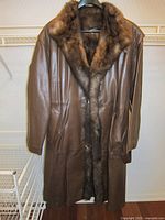 Full view of the brown leather fur lined coat hanging on a hanger, showing front button closure and fur collar.
