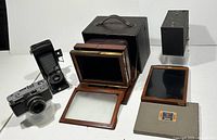 Four antique cameras displayed: wood plate extension camera with leather carrying case and glass plates, Kodak Junior Six-16 folding camera, Brownie box camera, Ansco Rokkor camera.