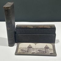 Black carrying case standing upright and laid flat with one stereoview card displayed in front showing the Chapel Bridge.