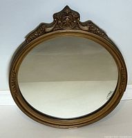 Full view of round antique mirror with gilded wooden frame and ornate top crest, showing overall condition and design details.