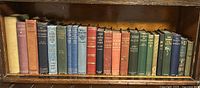 Shelf with 23 old hardcover books showing variety of colors and gilt spines.