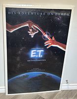 Front view of the framed E.T. The Extra-Terrestrial 1982 movie poster. Shows the fingerprint contact scene with Earth below and credits at the bottom.