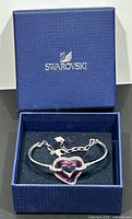 Blue Swarovski box with logo containing silver-tone bangle bracelet with fuchsia pink crystal heart centerpiece.