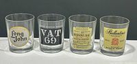 Four vintage Scotch whisky glasses in a row showing front logo designs of Long John, VAT 69, Hudson's Bay, and Ballantine's.