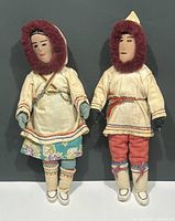 Full view of both vintage Inuit dolls in traditional clothing, standing side by side against a dark background.