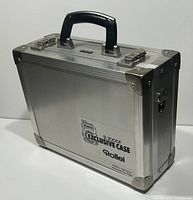 Front and side view of silver aluminum camera carrying case with black handle, metal corner reinforcements, latches and Rollei branding on side.