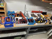 Overview of assorted tools in different plastic containers arranged on a metal shelf including wrenches, clamps, screwdrivers, and pliers.