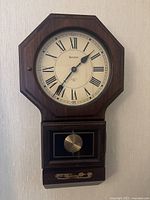 Full view of the antique Bulova wooden wall clock showing octagonal shape, dial, pendulum box, and decorative inlay.